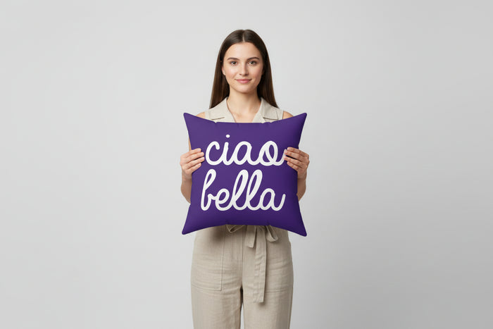 Woman holding a purple pillow with 'ciao bella' text on a plain background