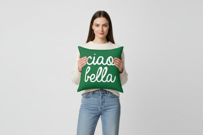 Woman holding a green pillow with 'ciao bella' text against a plain background