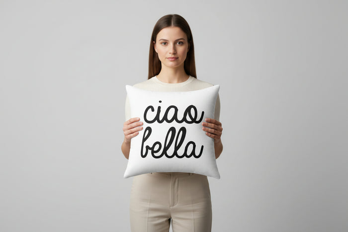 Woman holding a pillow with 'ciao bella' text against a plain background