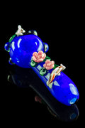 Angled close-up of the Empire Glassworks "Koi Pond" Spoon Pipe showing its deep blue glass, pink floral accents, and koi decoration against a black background