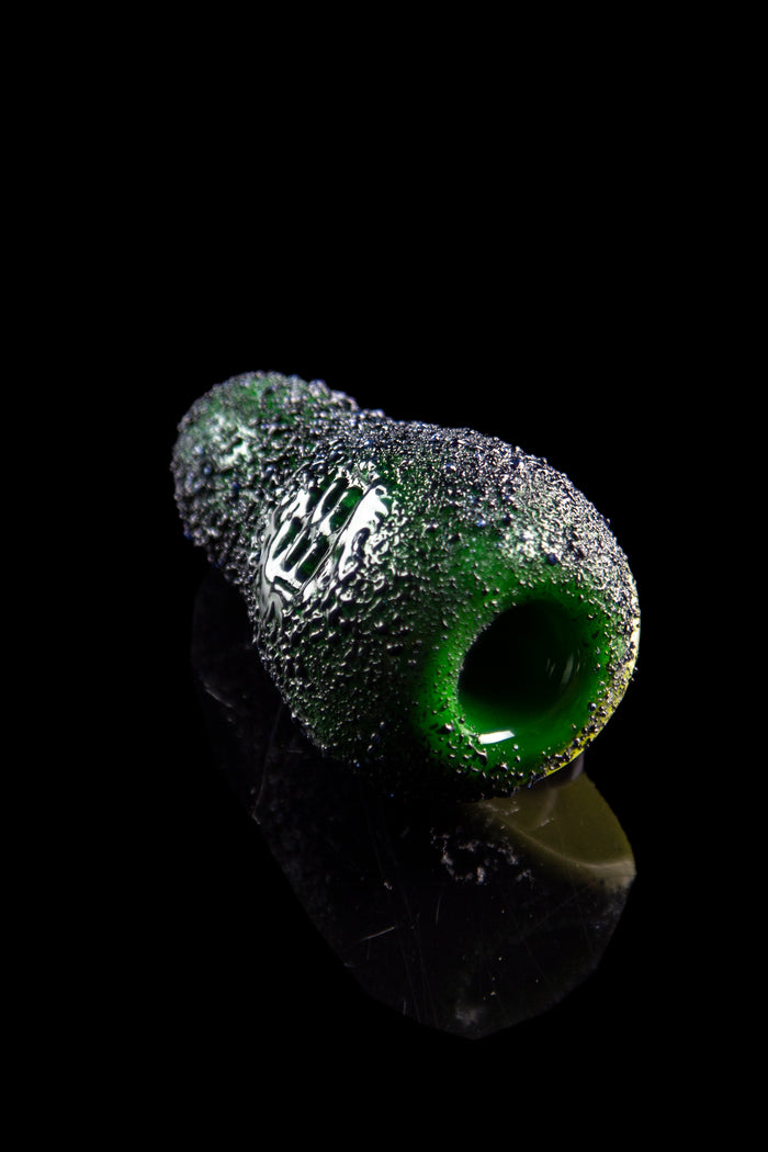 Green glass cannabis pipe with textured, speckled surface against a black background.