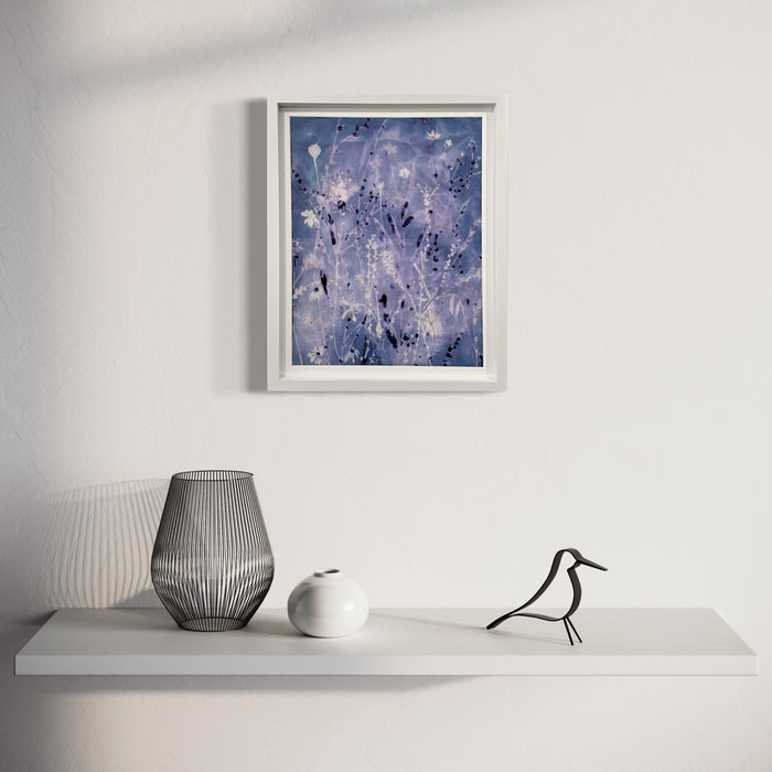 The artwork 'Iced Sky II' by Rachel Kohn features ethereal swirls of periwinkle and lavender hues, with splattered white accents resembling stars or frost crystals against a deep blue background. Created using dye, bleach, and acrylic on cotton, the abstract composition evokes a dreamy winter night sky with its flowing, organic patterns and celestial-inspired elements in a white frame.