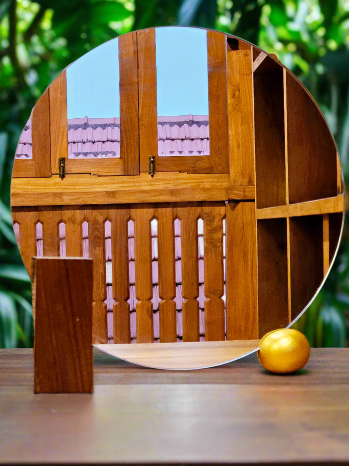 A round, reclaimed teak wood mirror with a geometric design, reflecting a portion of a wooden structure and an orange object, placed on a flat surface.