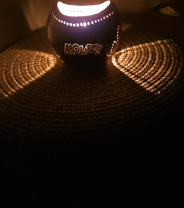 A lit tea light candle in a coconut shell holder with 'Mouzy' branding visible on the candle.