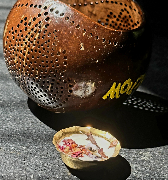 A lit tea light candle in a coconut shell holder with 'Mouzy' branding visible on the candle.