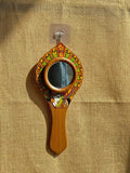 Decorative hand mirror with wooden handle and colorful frame on a beige fabric background