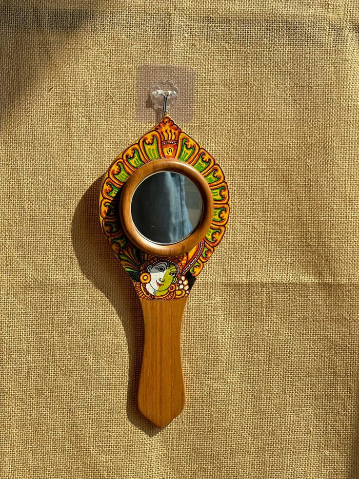 Decorative hand mirror with wooden handle and colorful frame on a beige fabric background