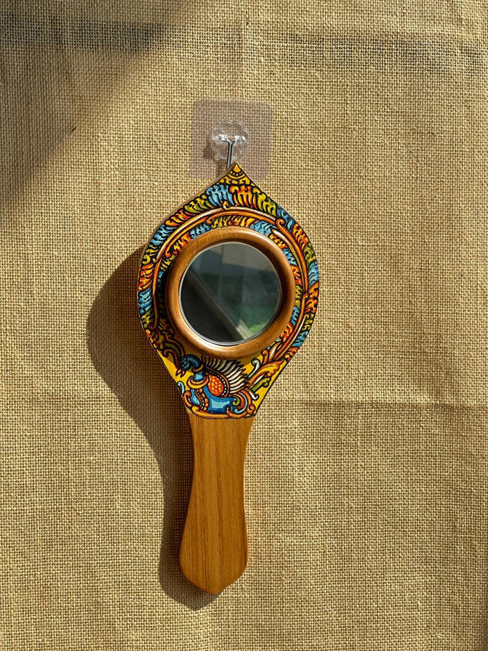 Decorative hand mirror with wooden handle and colorful frame on a textured beige background