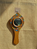 Decorative hand mirror with wooden handle and colorful frame on a textured beige background