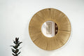 A round wall mirror with a golden aura created by radiating jute threads and a reflective iron frame, mounted on a white wall.