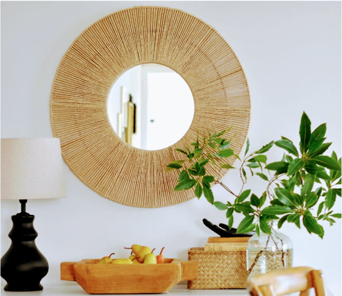A round wall mirror with a golden aura created by radiating jute threads and a reflective iron frame, mounted on a white wall.