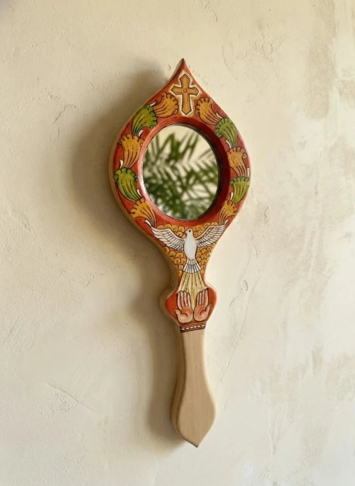 Decorative hand mirror with artistic design on a beige wall