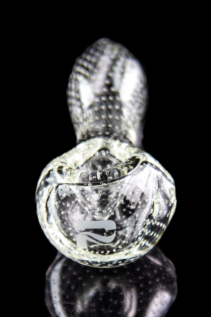 Clear glass cannabis oil rig with intricate bubble and swirl patterns, reflected on a black surface.
