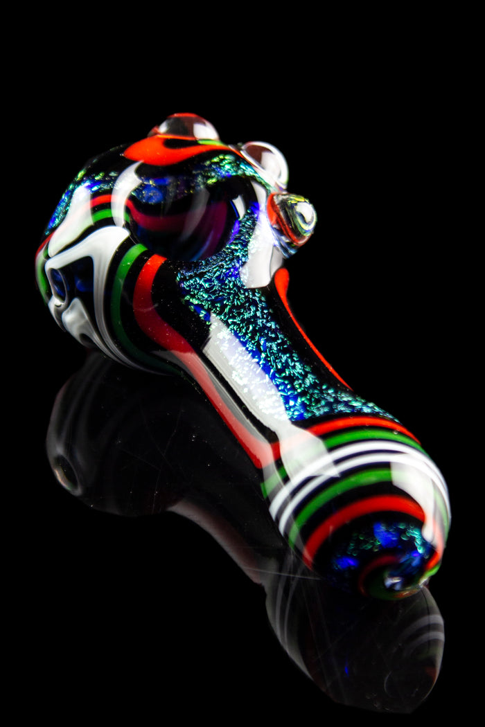 Hand-blown glass pipe with colorful stripes and speckled detailing, displayed against a black reflective surface.