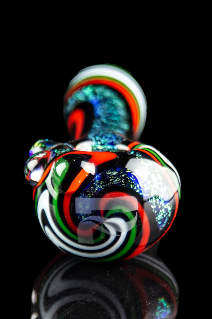 Hand-blown glass cannabis water pipe with vibrant swirling colors and glitter accents, reflecting on a dark surface.