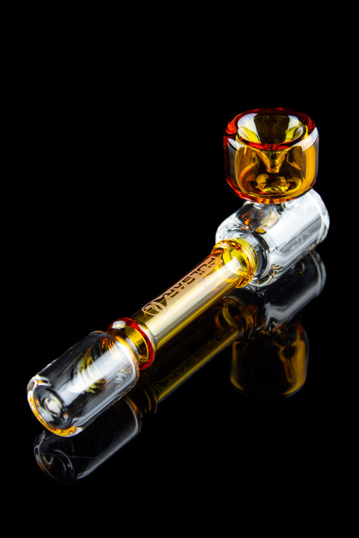 Glass cannabis pipe with amber and clear glass, reflected on a dark surface.