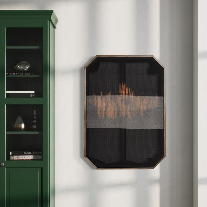 The artwork 'Untitled 104' by Victoria Manganiello features a striking abstract composition of copper-toned flame-like patterns woven across a dark charcoal mesh background, housed in an octagonal wooden frame. The textural interplay of natural and synthetic fibers creates a mesmerizing horizon effect against the minimalist black backdrop. The piece measures 30x42 inches and hangs beside an emerald green bookshelf.