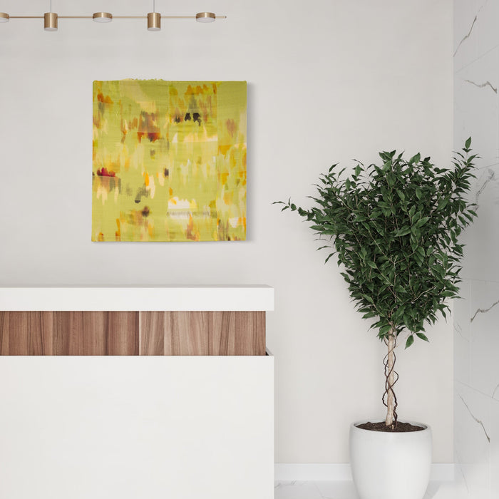 The artwork 'Untitled 13' by Victoria Manganiello features an abstract composition in vibrant yellow hues with scattered orange and brown accents. The textural woven piece combines natural and synthetic fibers creating a dynamic, brushstroke-like effect across the 38x36 inch canvas, displayed above a modern white cabinet beside a potted plant. By Victoria Manganiello.