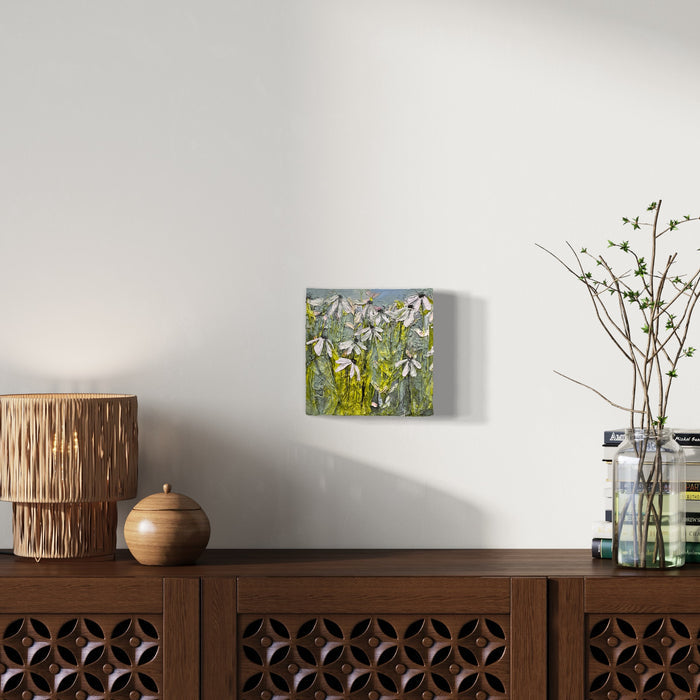 The artwork 'Wildflowers' by Rachel Kohn features delicate white blossoms dancing against a textured sage green background. Loose, impressionistic brushstrokes in acrylic paint capture the natural movement of wildflowers in a meadow. The 8x8 inch canvas showcases a harmonious blend of soft whites, earthy greens, and subtle blue undertones, creating a serene botanical composition by Rachel Kohn.